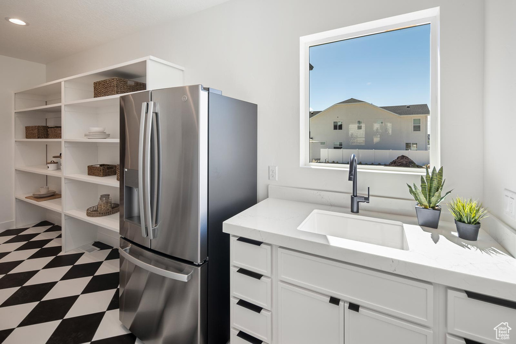 Kitchen with stainless steel refrigerator with ice dispenser, light stone counters, tile flooring, white cabinetry, and sink