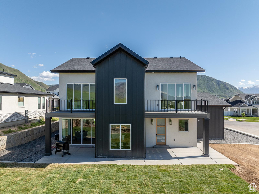 Back of house featuring a patio, a mountain view, a balcony, and a lawn