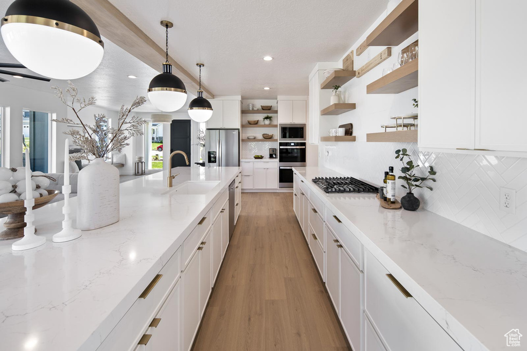 Kitchen with stainless steel appliances, decorative light fixtures, light wood-type flooring, sink, and white cabinets