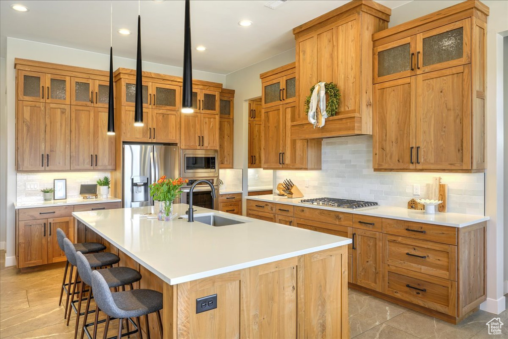 Kitchen with a kitchen bar, appliances with stainless steel finishes, backsplash, an island with sink, and sink