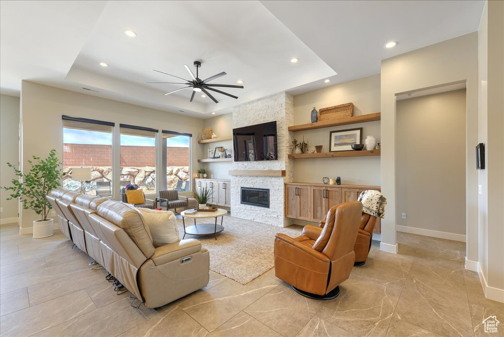 Living room featuring ceiling fan, light tile floors, a fireplace, and a tray ceiling