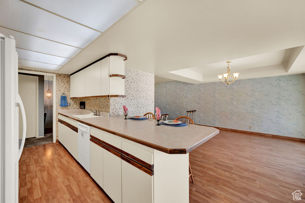 Kitchen with kitchen peninsula, backsplash, light hardwood / wood-style flooring, white appliances, and white cabinets