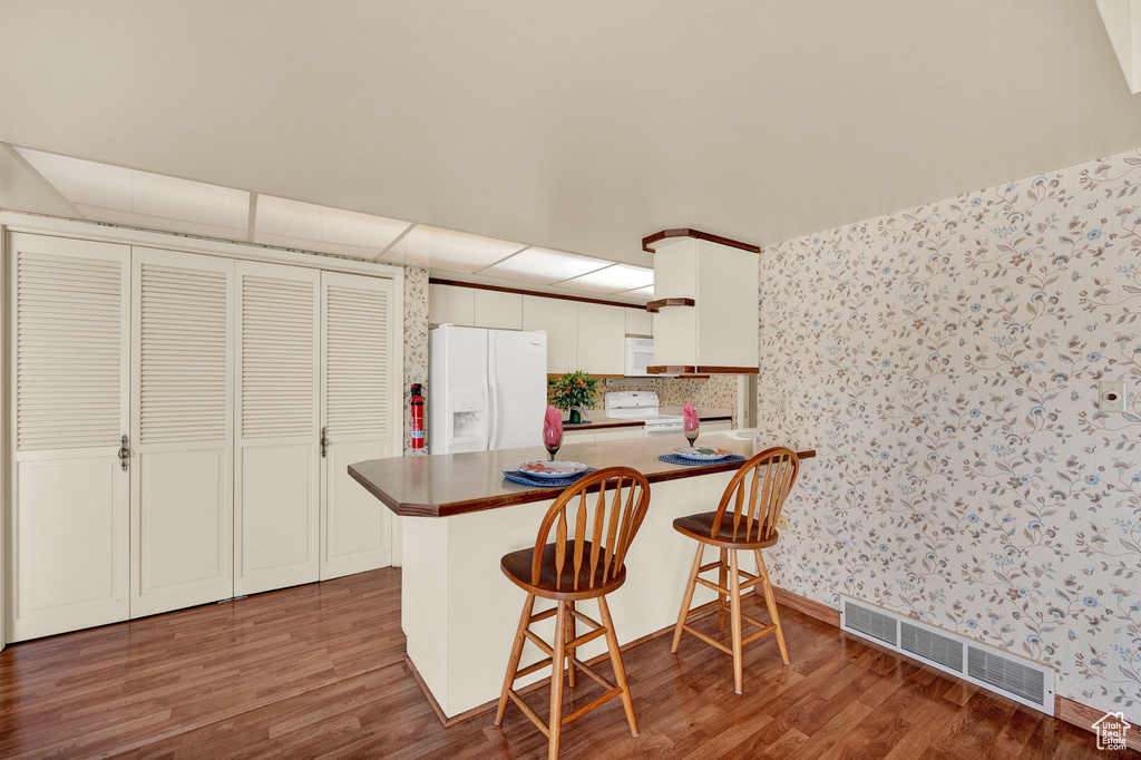 Kitchen featuring a kitchen bar, white cabinets, white appliances, dark hardwood / wood-style floors, and kitchen peninsula