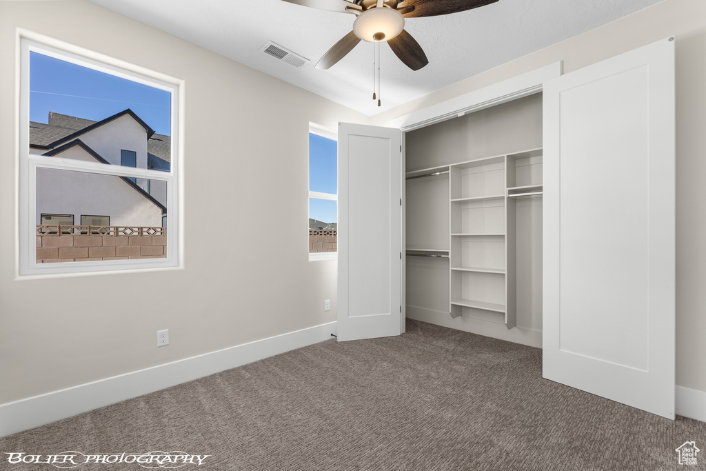 Unfurnished bedroom with a closet, dark colored carpet, ceiling fan, and multiple windows