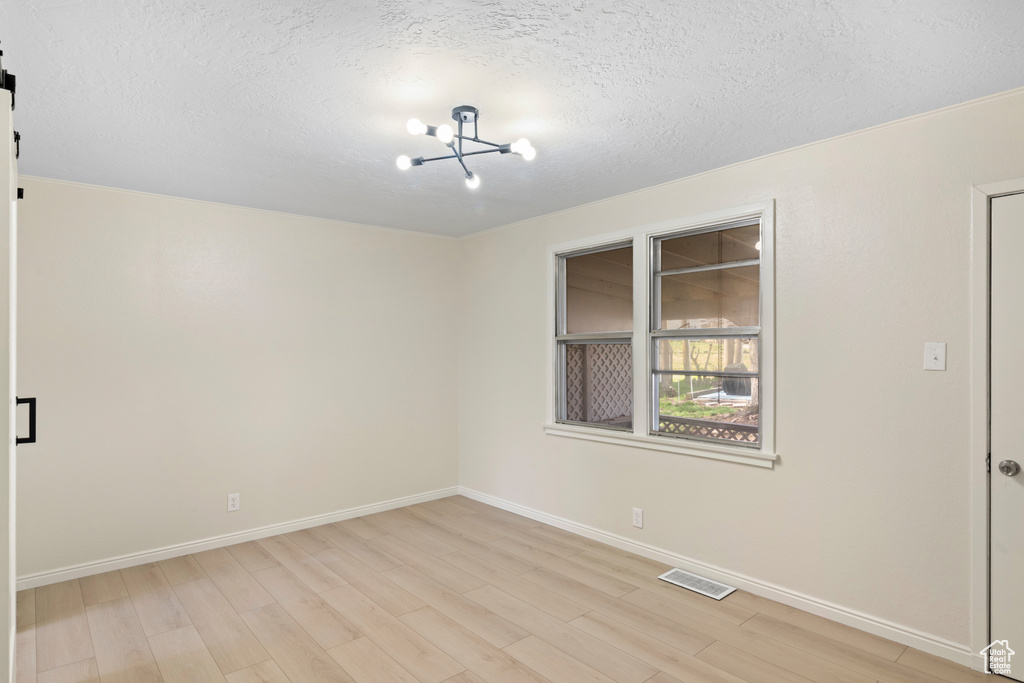 Unfurnished room with a chandelier, a textured ceiling, and light wood-type flooring