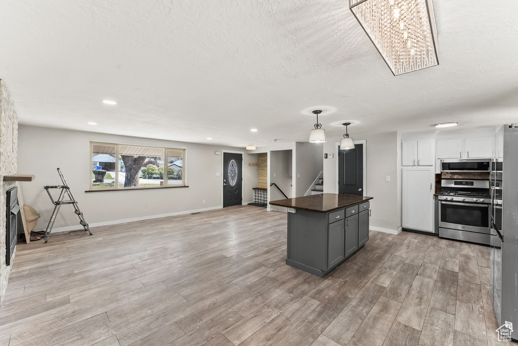 Kitchen with decorative light fixtures, white cabinets, light hardwood / wood-style flooring, a chandelier, and appliances with stainless steel finishes