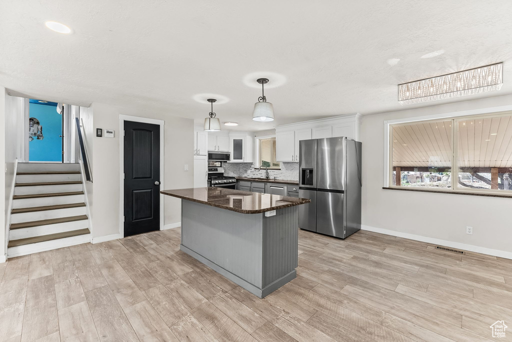 Kitchen with hanging light fixtures, white cabinets, light hardwood / wood-style flooring, appliances with stainless steel finishes, and tasteful backsplash