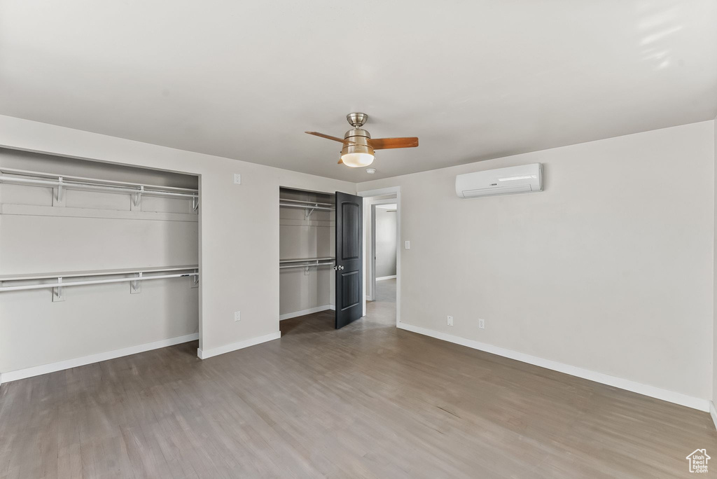 Unfurnished bedroom with multiple closets, ceiling fan, a wall mounted AC, and dark hardwood / wood-style flooring