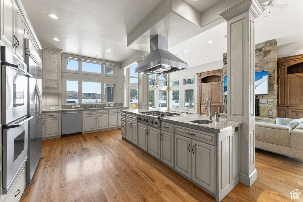 Kitchen with gray cabinets, ceiling fan, stainless steel appliances, island range hood, and light wood-type flooring