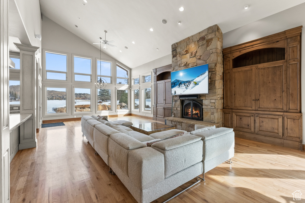 Living room featuring high vaulted ceiling, a water view, ceiling fan, a fireplace, and light wood-type flooring