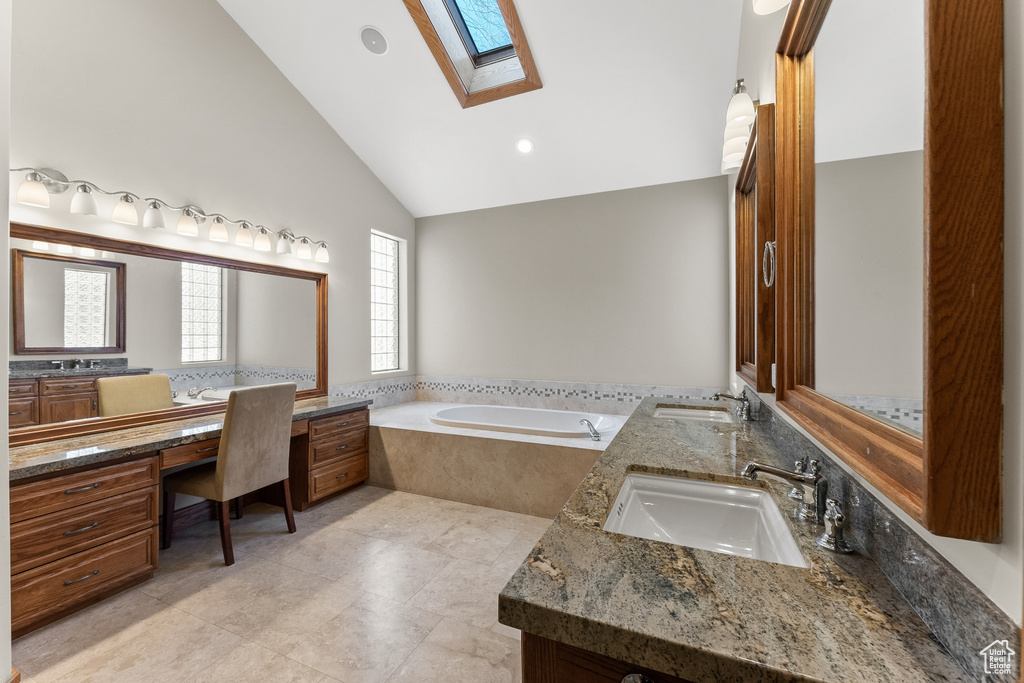 Bathroom featuring a skylight, tile flooring, double sink vanity, high vaulted ceiling, and tiled bath