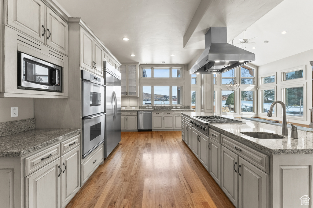 Kitchen with built in appliances, gray cabinets, island range hood, light stone counters, and light hardwood / wood-style floors