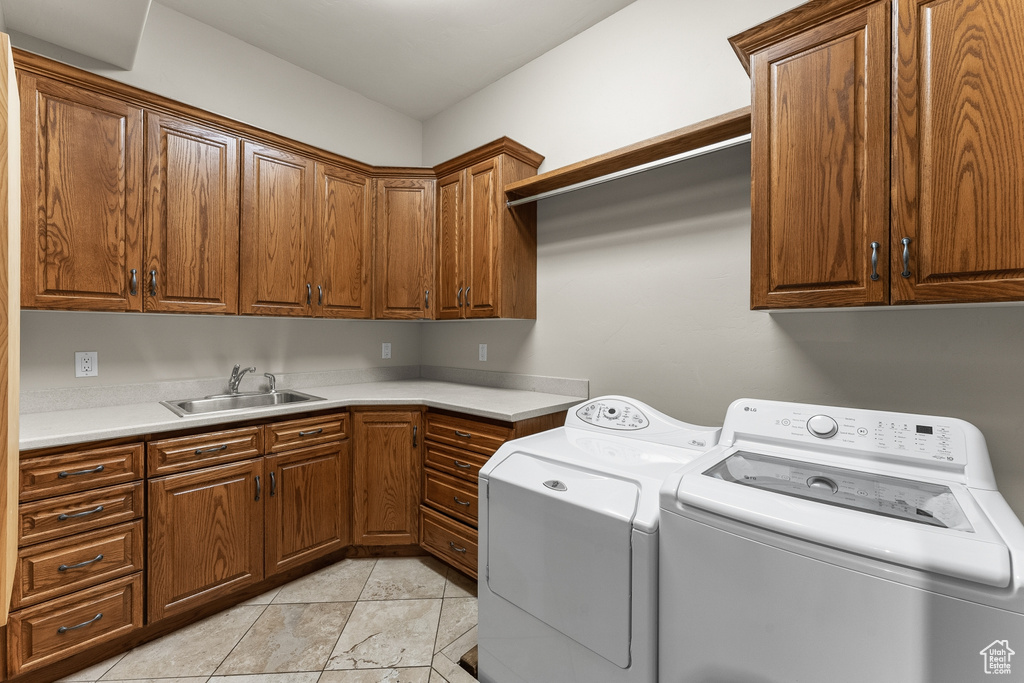 Clothes washing area with cabinets, washing machine and clothes dryer, light tile floors, and sink