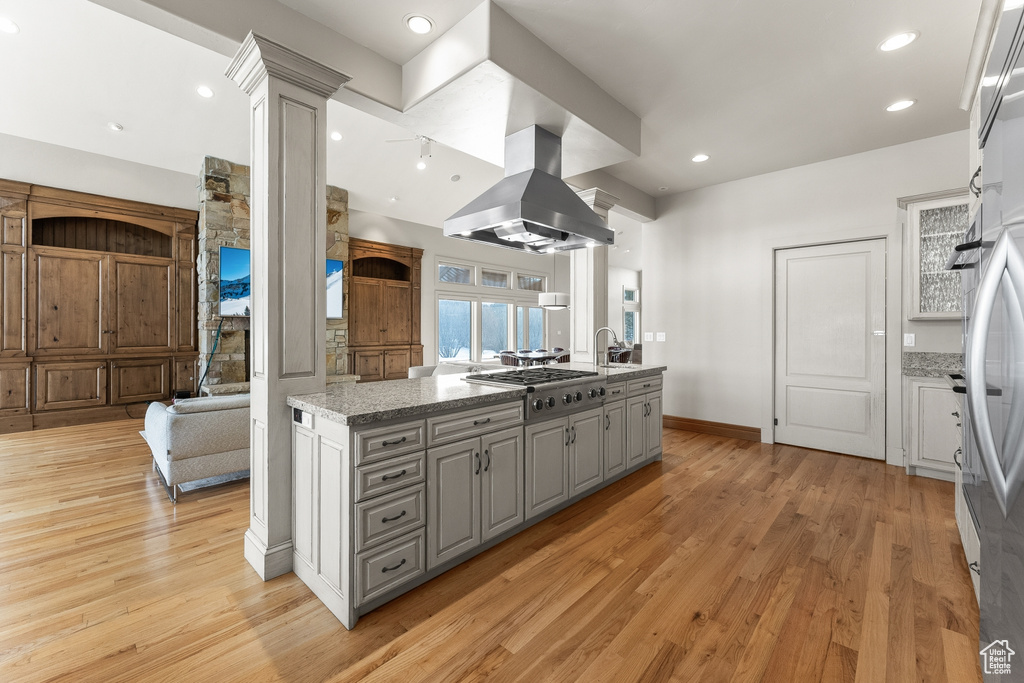Kitchen with stainless steel gas stovetop, light wood-type flooring, gray cabinets, island range hood, and light stone countertops