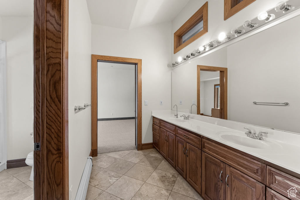 Bathroom with toilet, tile floors, a baseboard heating unit, and double sink vanity