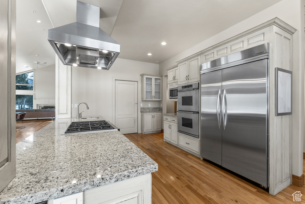 Kitchen featuring light stone counters, light hardwood / wood-style floors, island range hood, and built in appliances