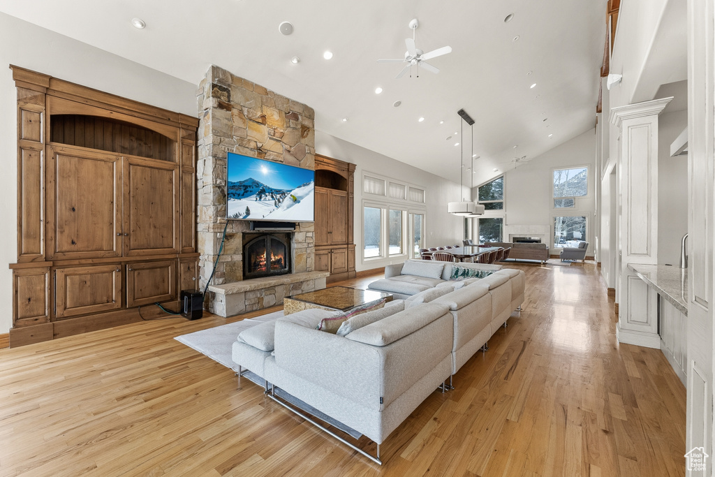 Living room featuring high vaulted ceiling, light hardwood / wood-style floors, ceiling fan, and a fireplace