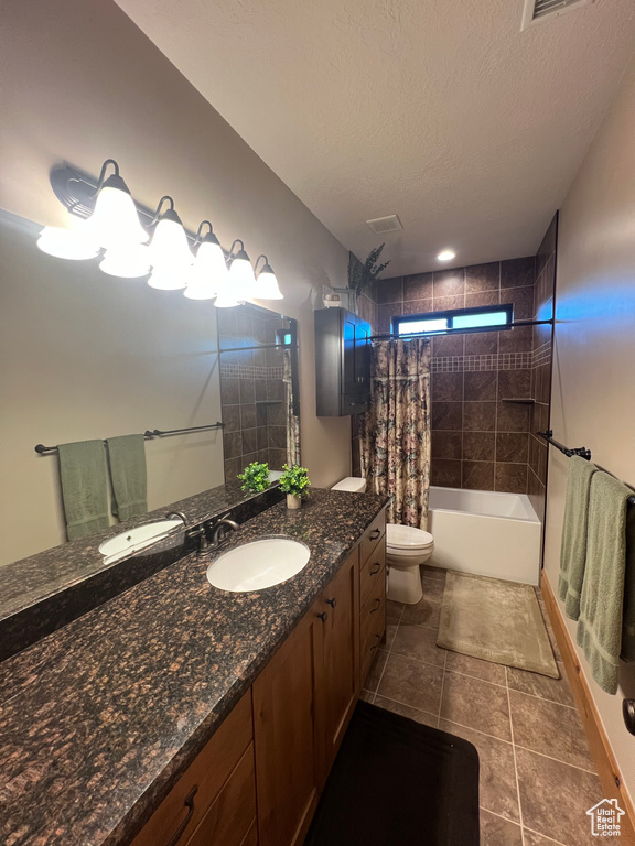 Full bathroom with vanity with extensive cabinet space, shower / tub combo with curtain, tile flooring, toilet, and a textured ceiling