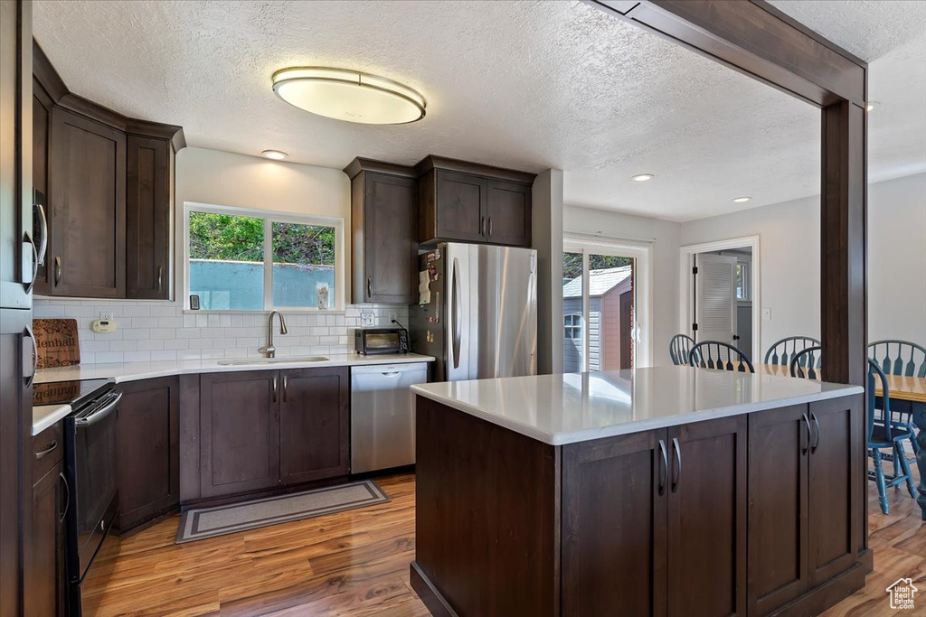 Kitchen featuring appliances with stainless steel finishes, sink, backsplash, dark brown cabinets, and wood-type flooring