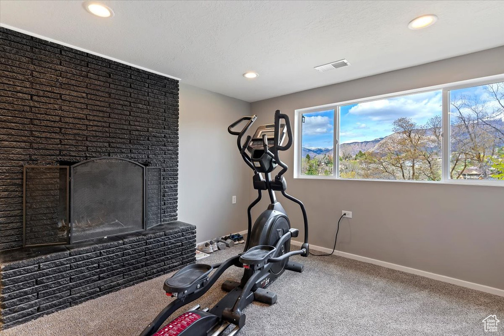 Exercise area featuring a healthy amount of sunlight, a fireplace, and dark carpet