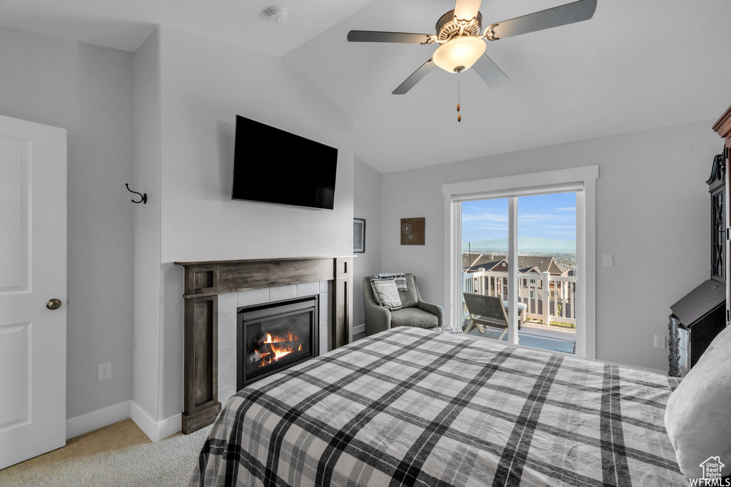 Bedroom featuring light colored carpet, access to exterior, ceiling fan, a fireplace, and vaulted ceiling