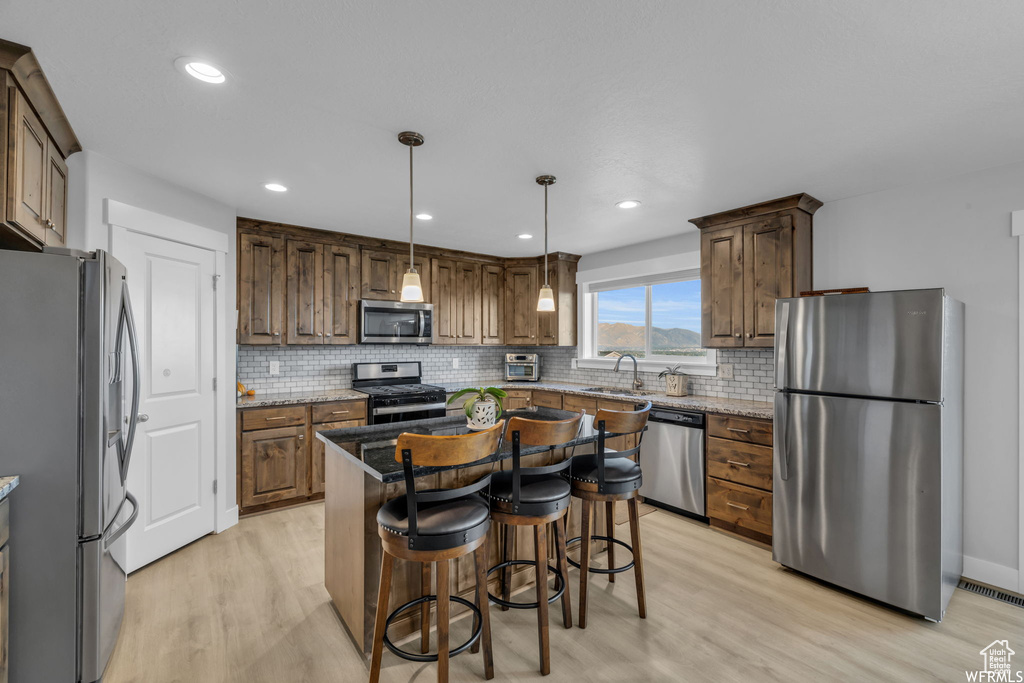 Kitchen featuring light hardwood / wood-style floors, stainless steel appliances, dark stone counters, and a center island