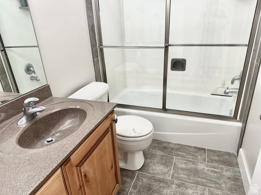 Full bathroom with oversized vanity, combined bath / shower with glass door, tile floors, and toilet