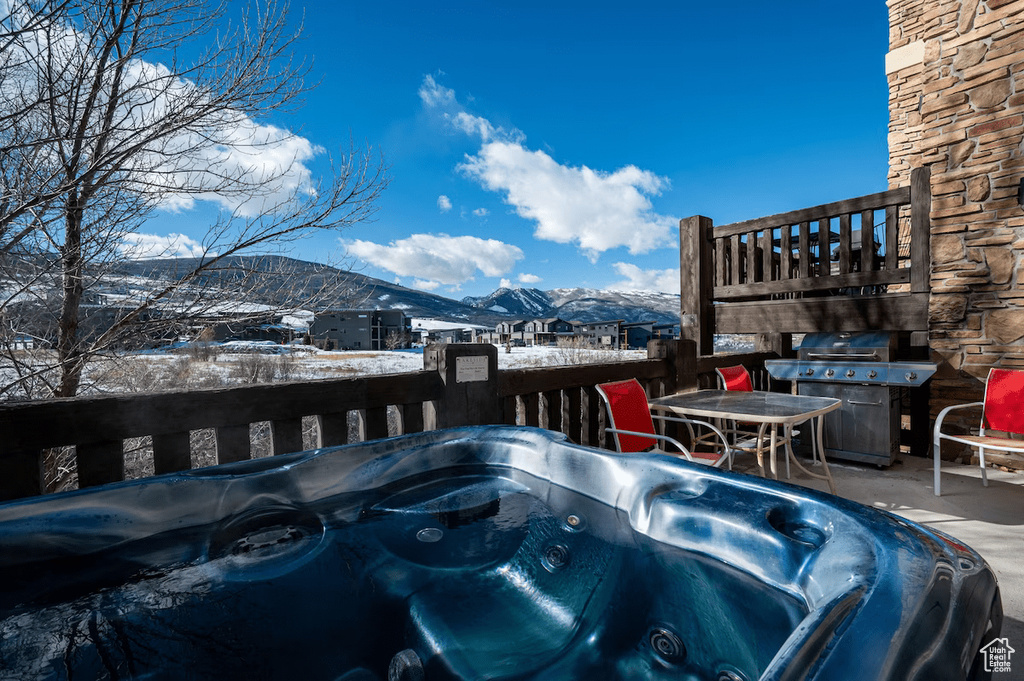 Snow covered pool with a hot tub, a mountain view, and grilling area
