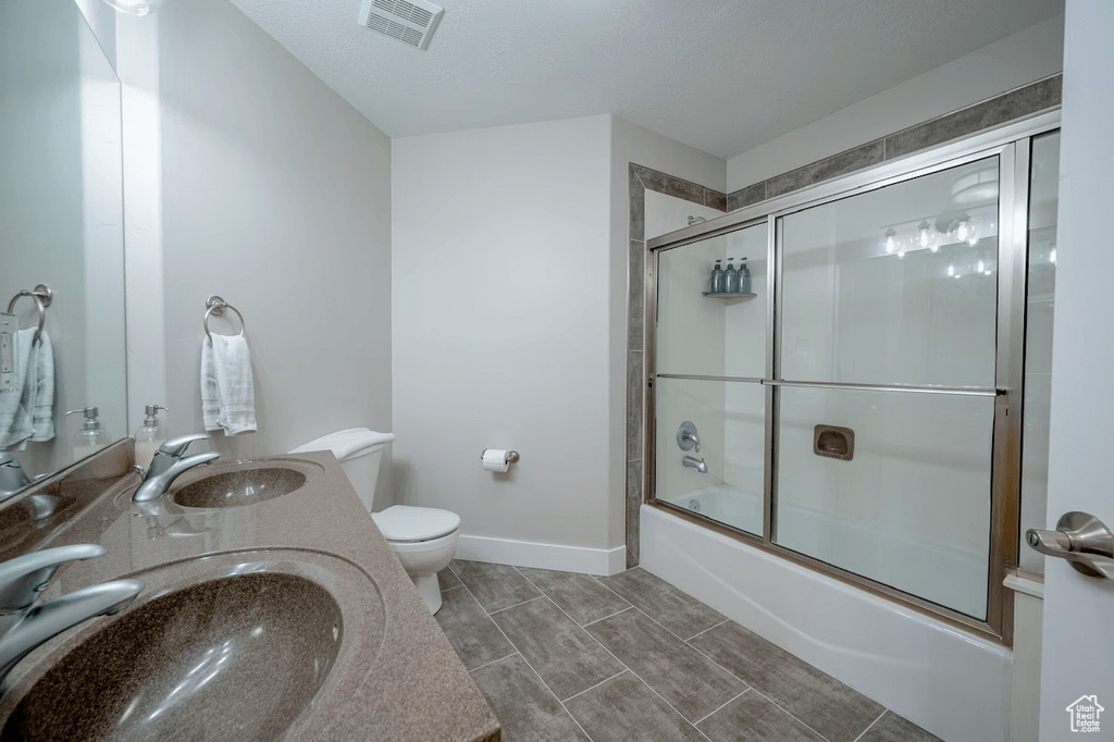 Full bathroom featuring dual sinks, toilet, tile floors, and bath / shower combo with glass door