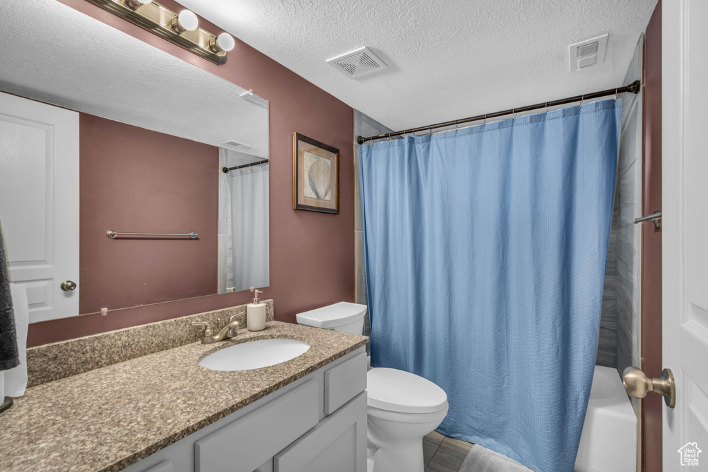 Full bathroom with a textured ceiling, toilet, vanity with extensive cabinet space, and tile floors
