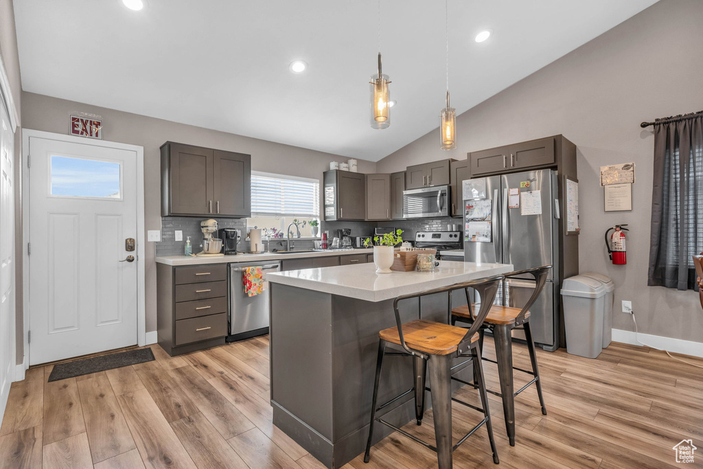 Kitchen featuring appliances with stainless steel finishes, light hardwood / wood-style flooring, lofted ceiling, a kitchen island, and tasteful backsplash