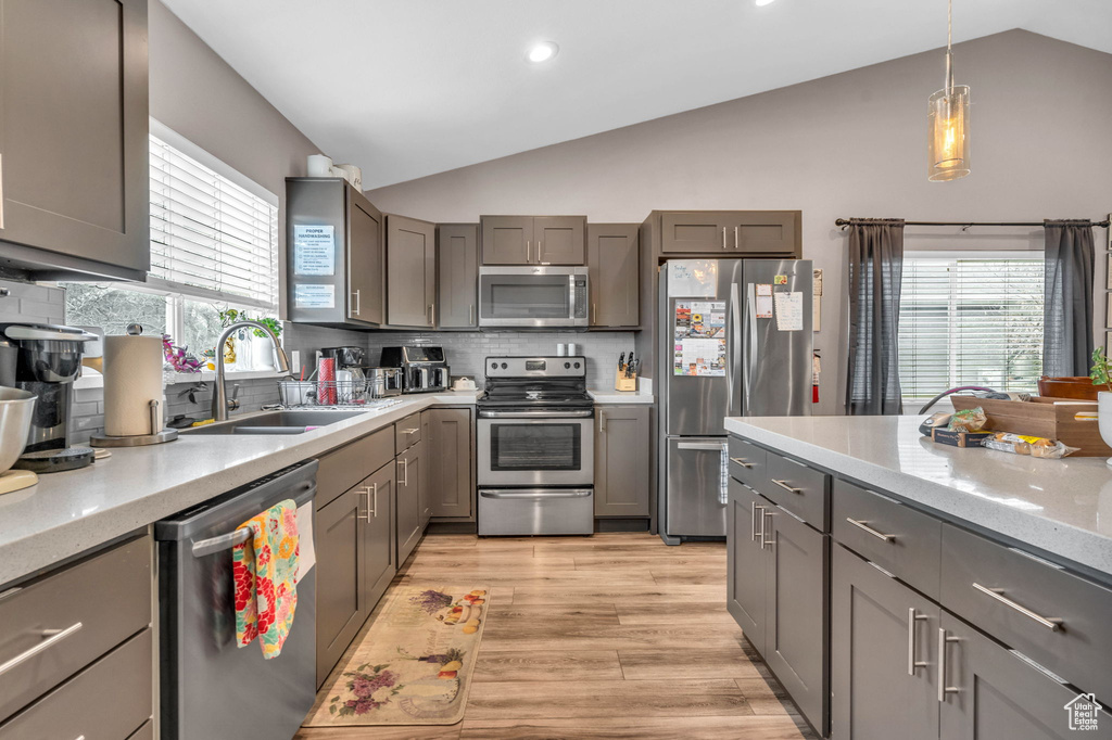 Kitchen featuring appliances with stainless steel finishes, tasteful backsplash, vaulted ceiling, sink, and light hardwood / wood-style flooring