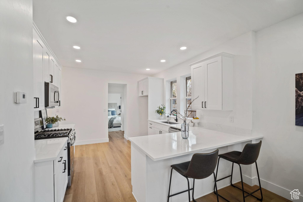 Kitchen featuring kitchen peninsula, stainless steel appliances, light hardwood / wood-style floors, white cabinets, and a kitchen breakfast bar