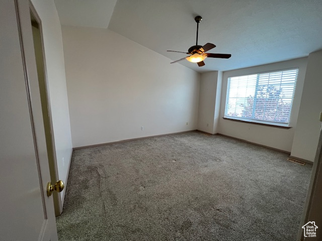 Spare room featuring light colored carpet, vaulted ceiling, and ceiling fan