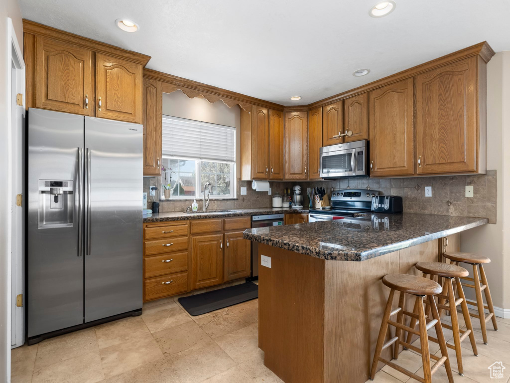 Kitchen with appliances with stainless steel finishes, backsplash, light tile flooring, sink, and a breakfast bar