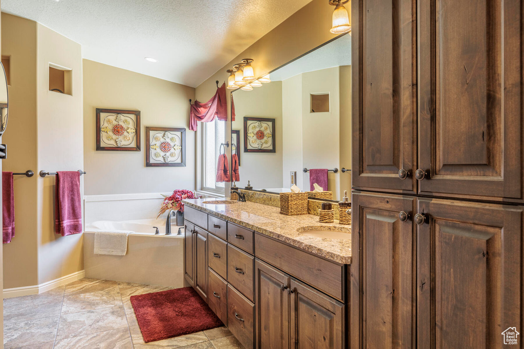Bathroom featuring a textured ceiling, tile floors, a washtub, and double vanity