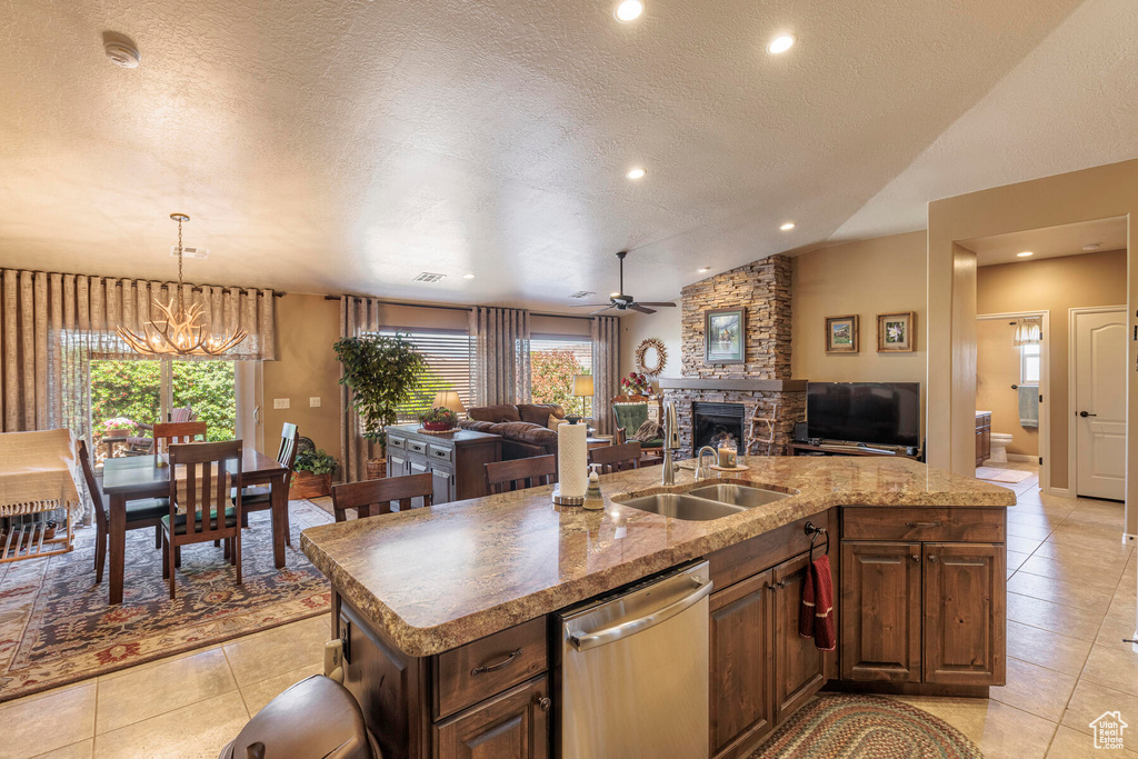 Kitchen with a kitchen island with sink, a fireplace, vaulted ceiling, dishwasher, and a textured ceiling