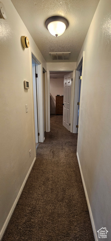 Hallway featuring dark carpet and a textured ceiling