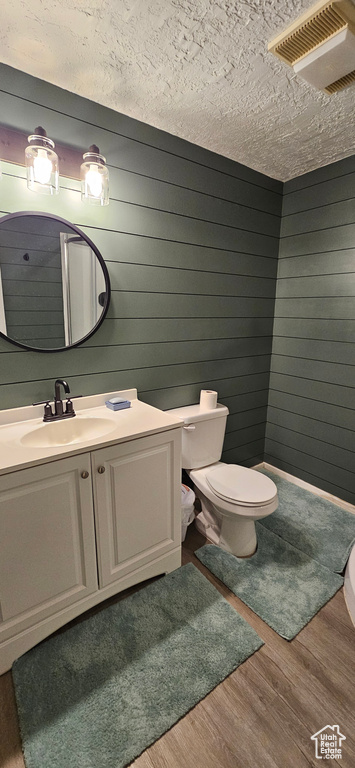Bathroom featuring a textured ceiling, toilet, wood walls, vanity, and hardwood / wood-style flooring