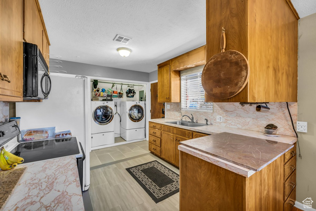 Kitchen with a textured ceiling, sink, tasteful backsplash, white range with electric stovetop, and separate washer and dryer