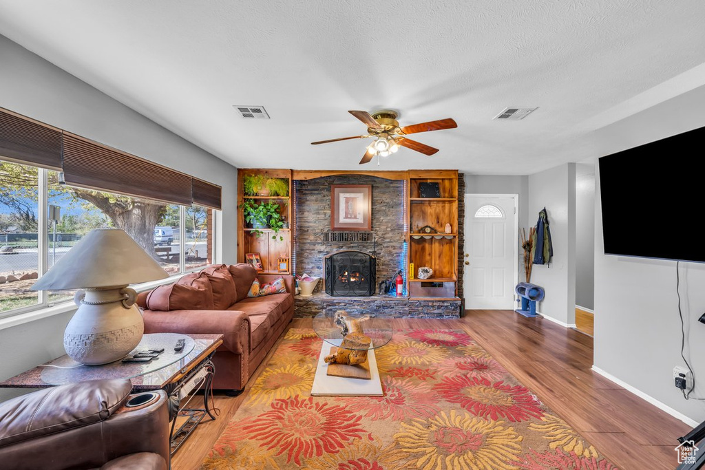 Living room featuring a stone fireplace, a healthy amount of sunlight, ceiling fan, and light wood-type flooring