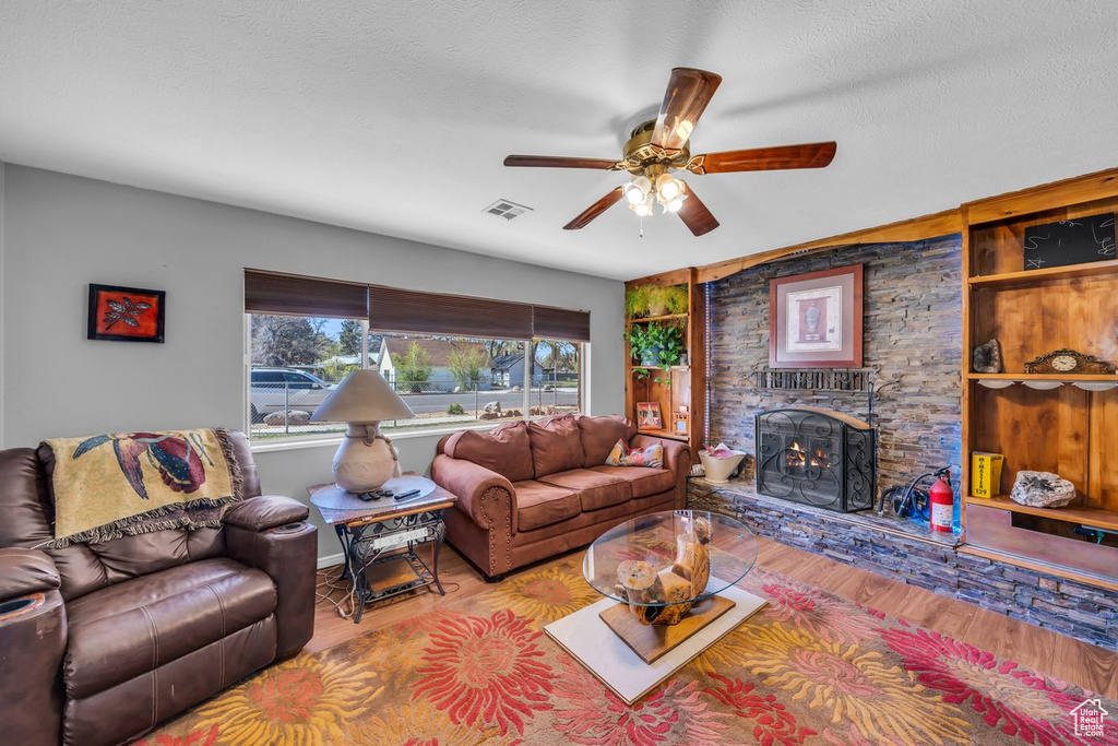 Living room with a textured ceiling, ceiling fan, light hardwood / wood-style floors, and a stone fireplace