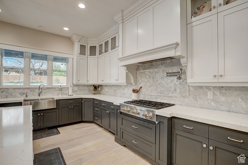 Kitchen with white cabinets, tasteful backsplash, light wood-type flooring, stainless steel gas cooktop, and light stone countertops
