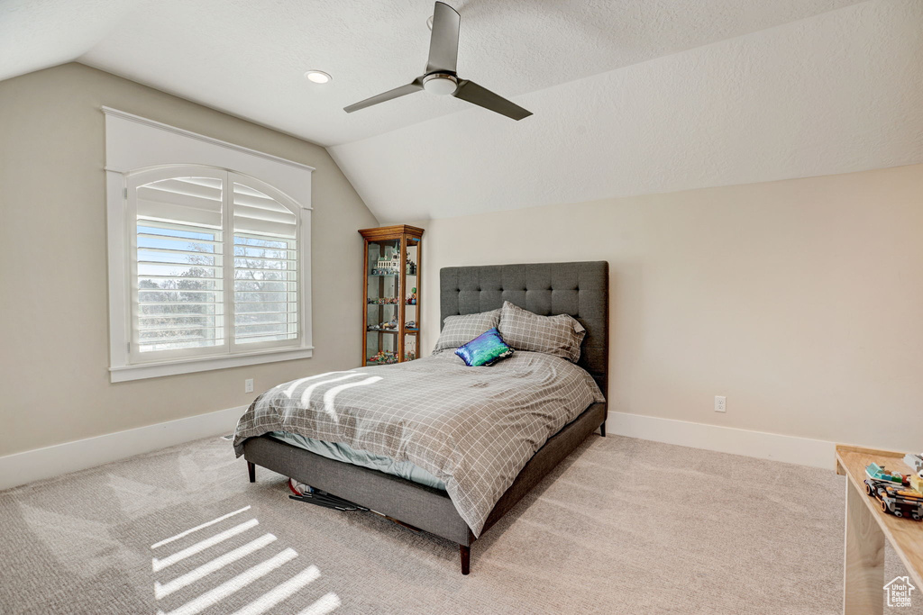Bedroom with light colored carpet, a textured ceiling, ceiling fan, and vaulted ceiling