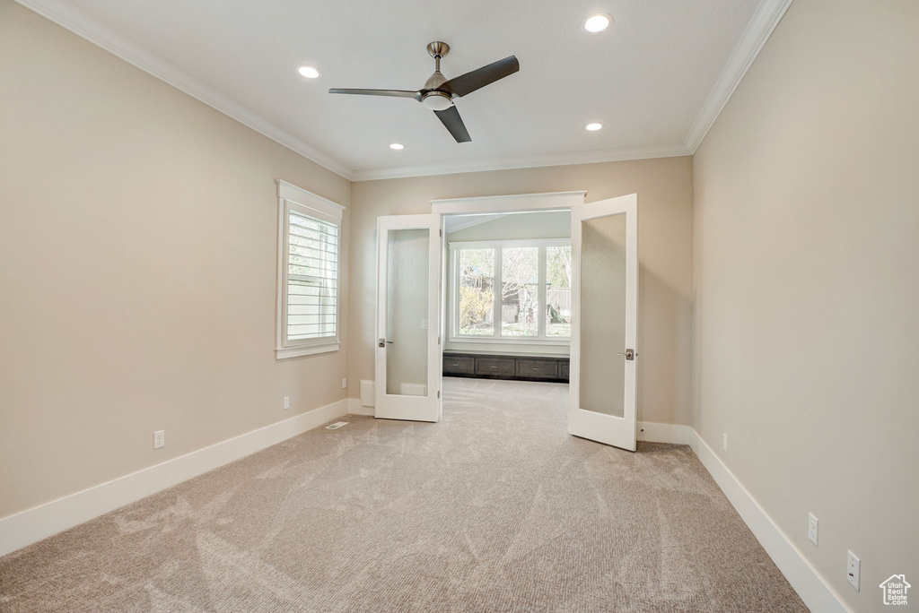 Unfurnished bedroom featuring light carpet, ornamental molding, ceiling fan, and french doors