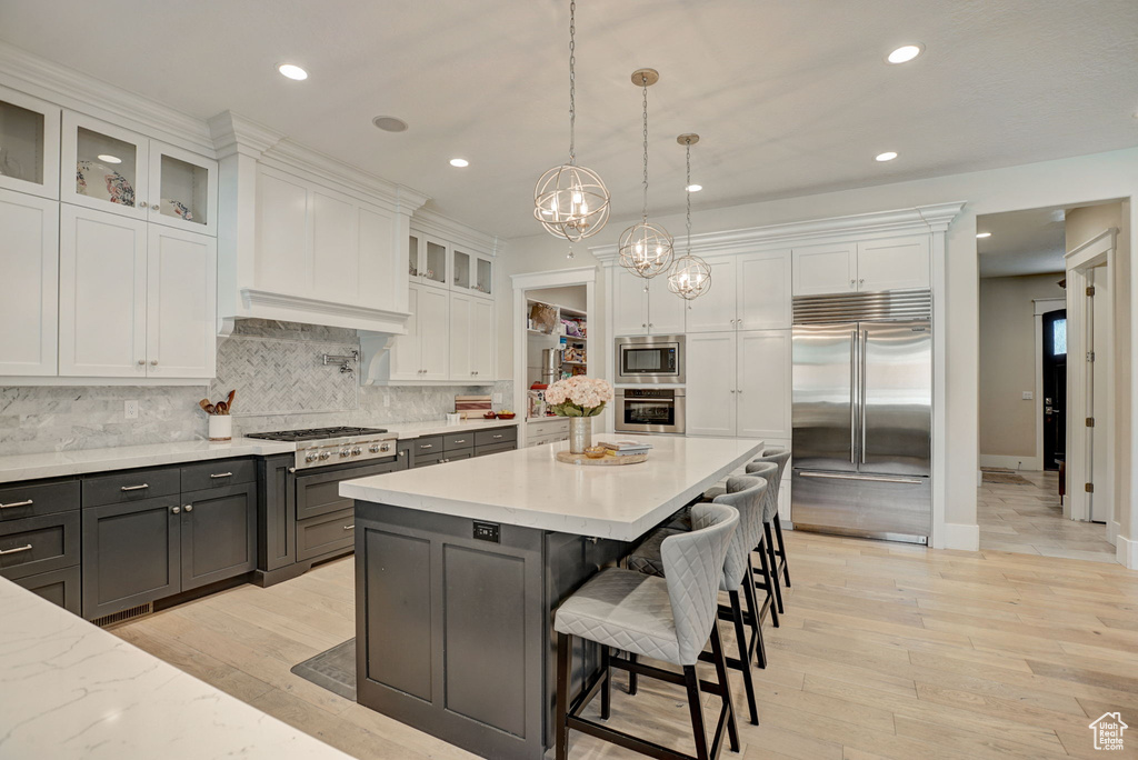 Kitchen with built in appliances, hanging light fixtures, tasteful backsplash, white cabinetry, and a kitchen breakfast bar