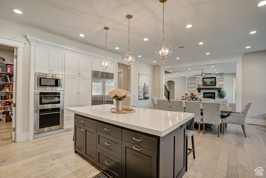 Kitchen featuring built in appliances, decorative light fixtures, a stone fireplace, light hardwood / wood-style flooring, and white cabinetry