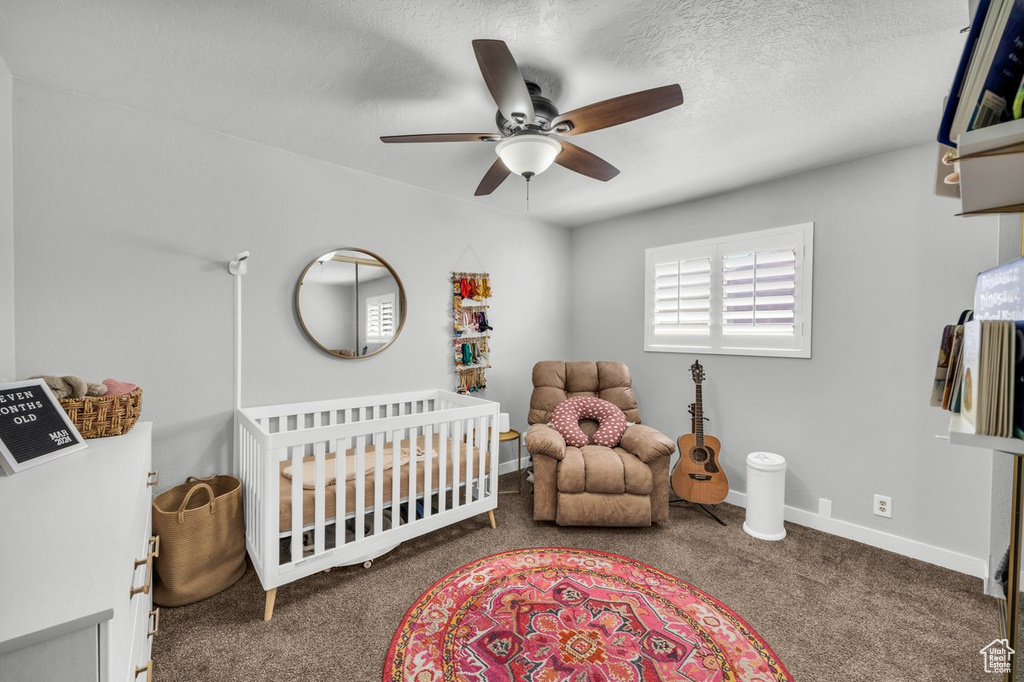 Bedroom with a textured ceiling, ceiling fan, a nursery area, and dark colored carpet