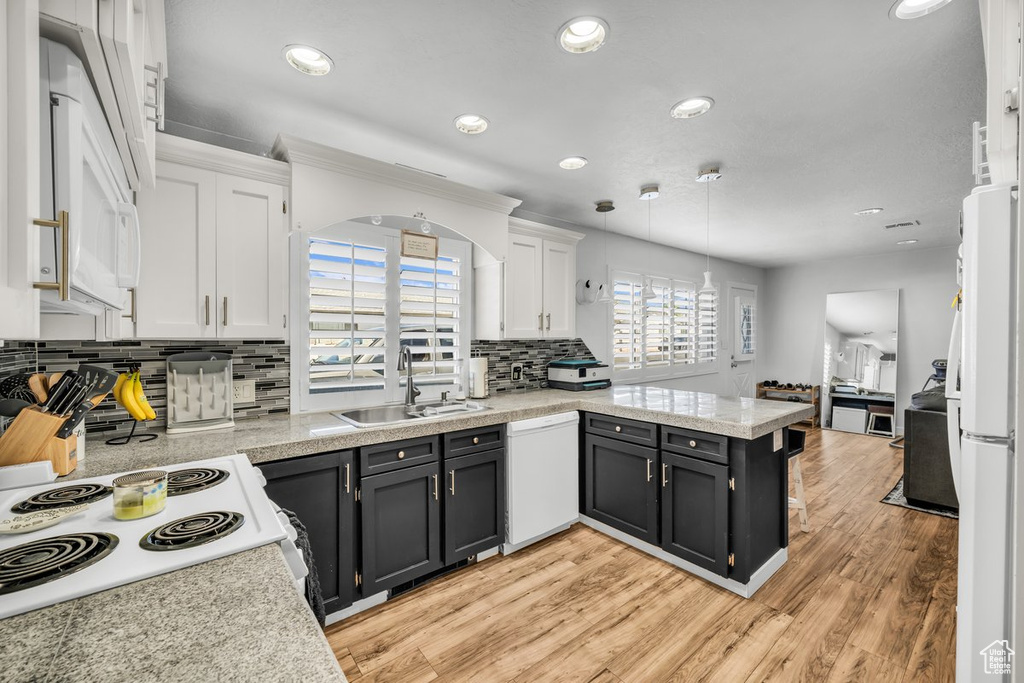 Kitchen with backsplash, white appliances, white cabinetry, sink, and light wood-type flooring