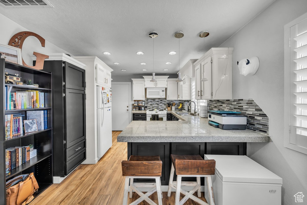 Kitchen with decorative light fixtures, white appliances, kitchen peninsula, a kitchen bar, and tasteful backsplash